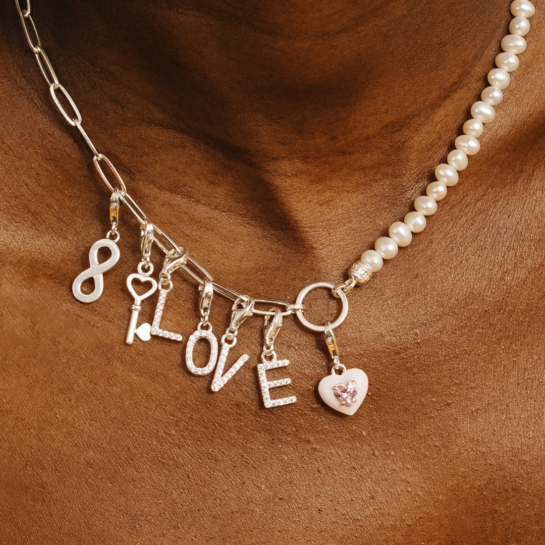 Sterling silver charm necklace combining paperclip chain and freshwater pearls, with LOVE letter, infinity, key, and heart charms.