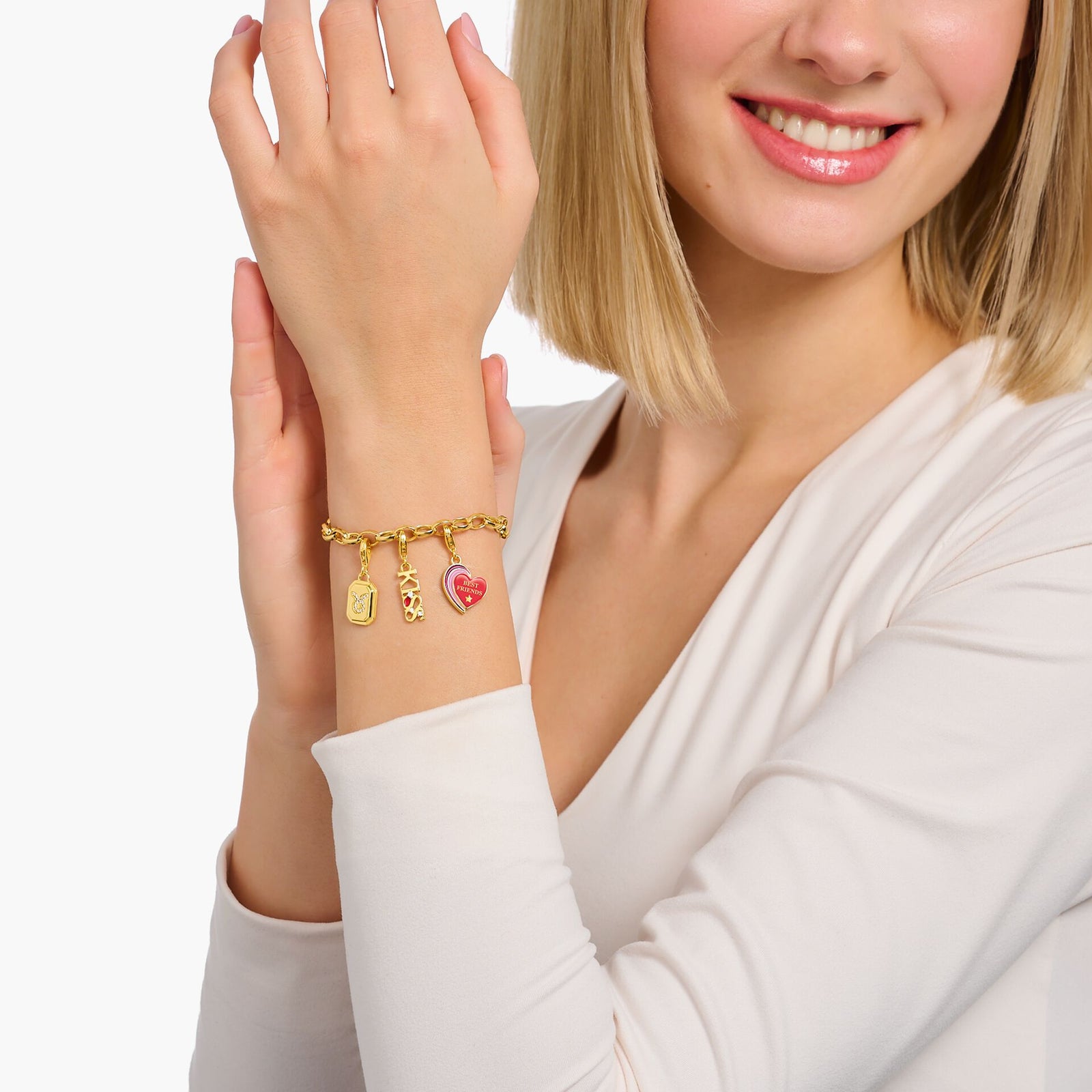 Woman wearing a gold-plated charm bracelet with a "Best Friends" heart, floral, and tag charms on her wrist.