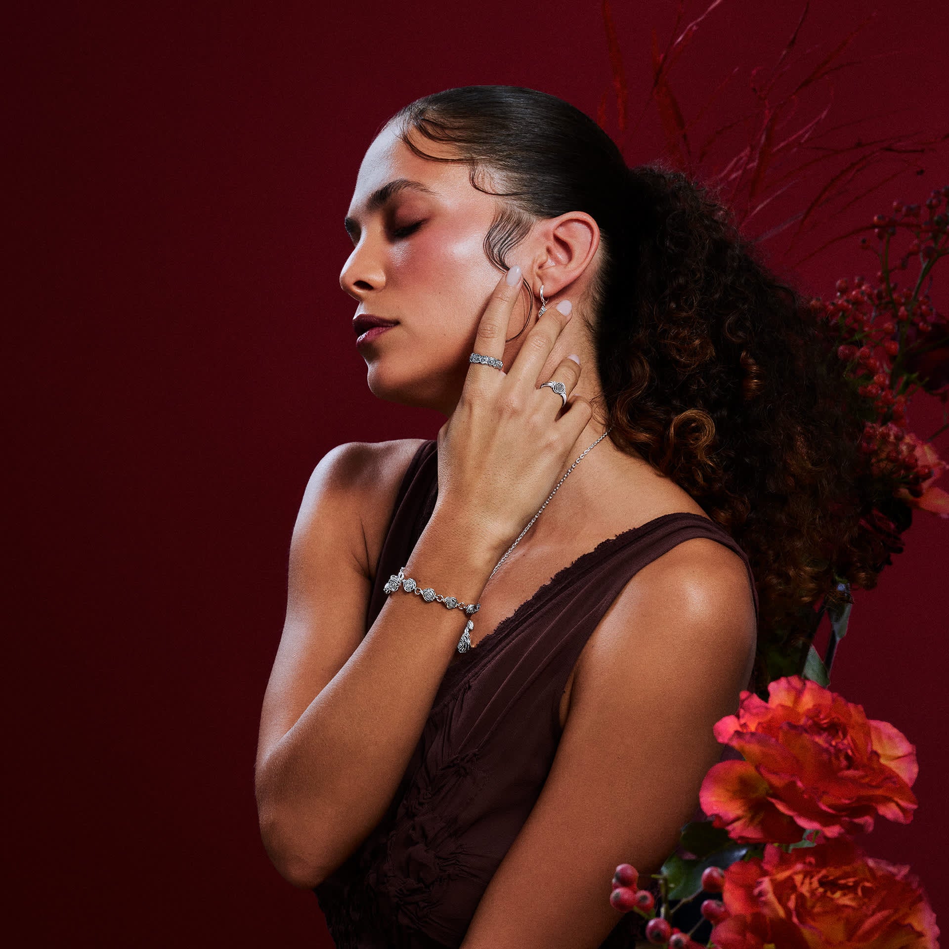 Woman wearing THOMAS SABO sterling silver hoop earrings, eternity ring, pendant necklace and bracelet against a deep red background.