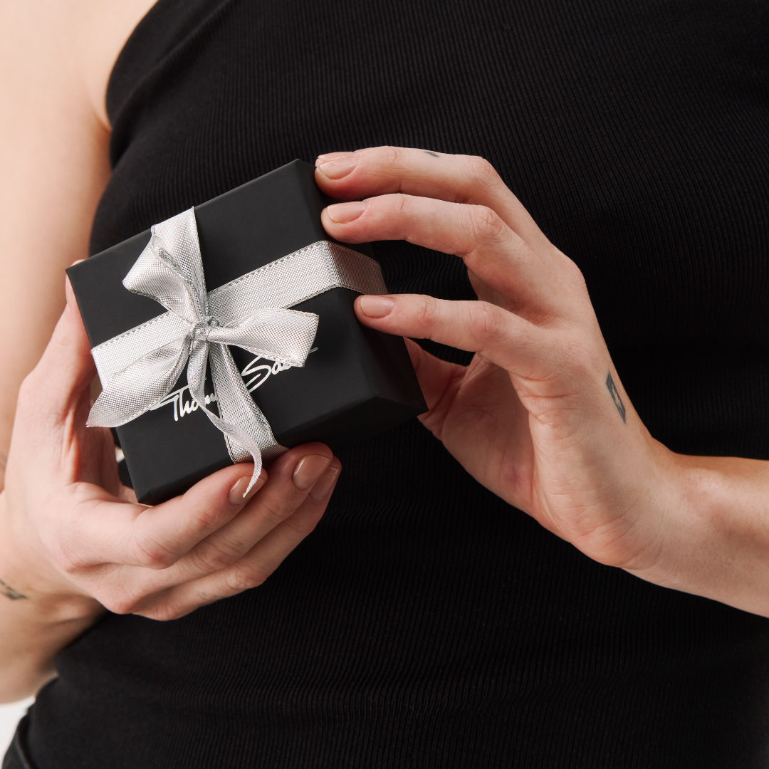 Smiling woman holding a THOMAS SABO gift box, wearing a delicate silver necklace with pearl pendant and silver bracelet.