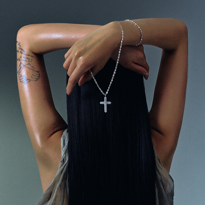 Woman seen from behind showcasing a THOMAS SABO crystal-pavé cross pendant necklace and silver bracelets, with dark hair and arm tattoo.