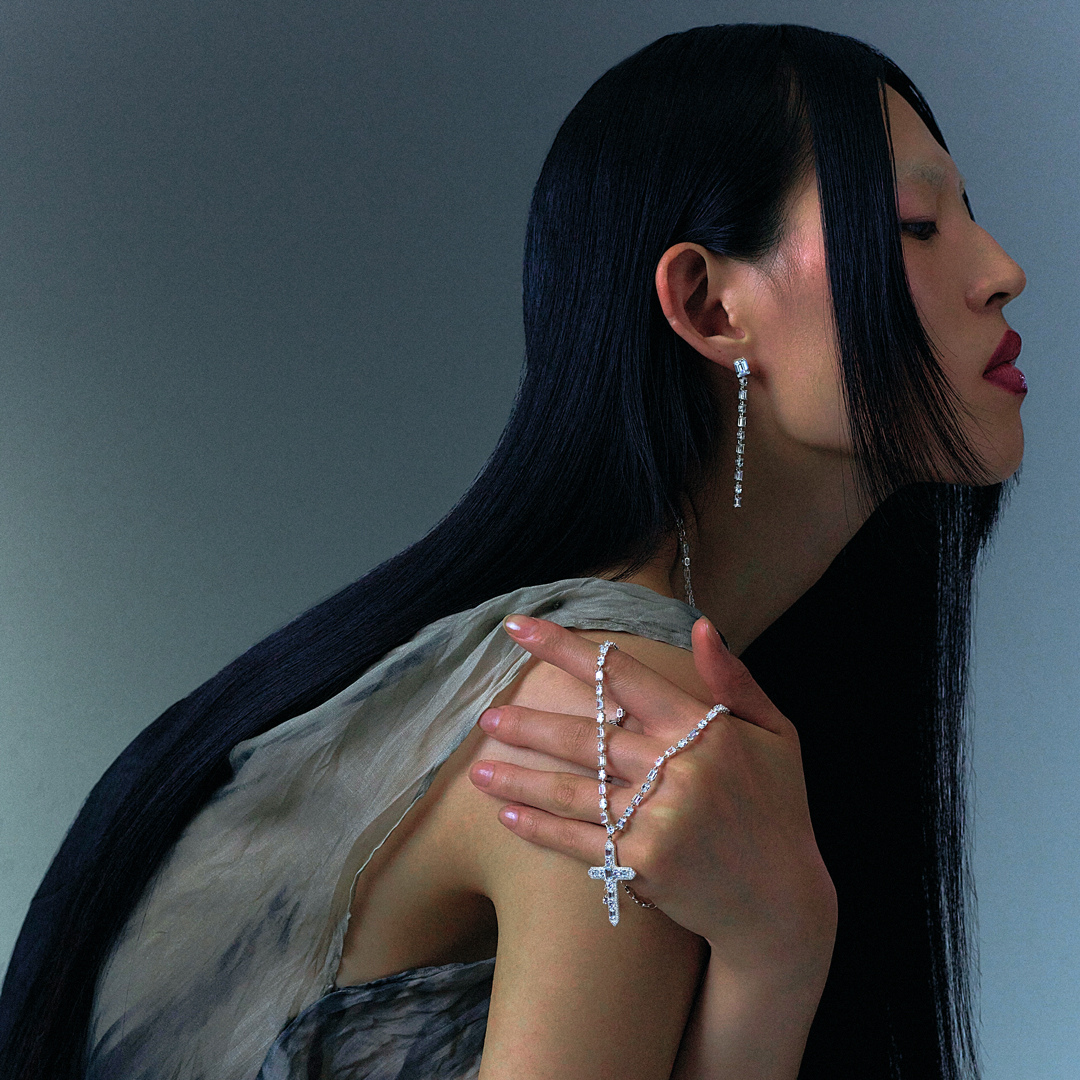 Woman seen from behind showcasing a THOMAS SABO crystal-pavé cross pendant necklace and silver bracelets, with dark hair and arm tattoo.