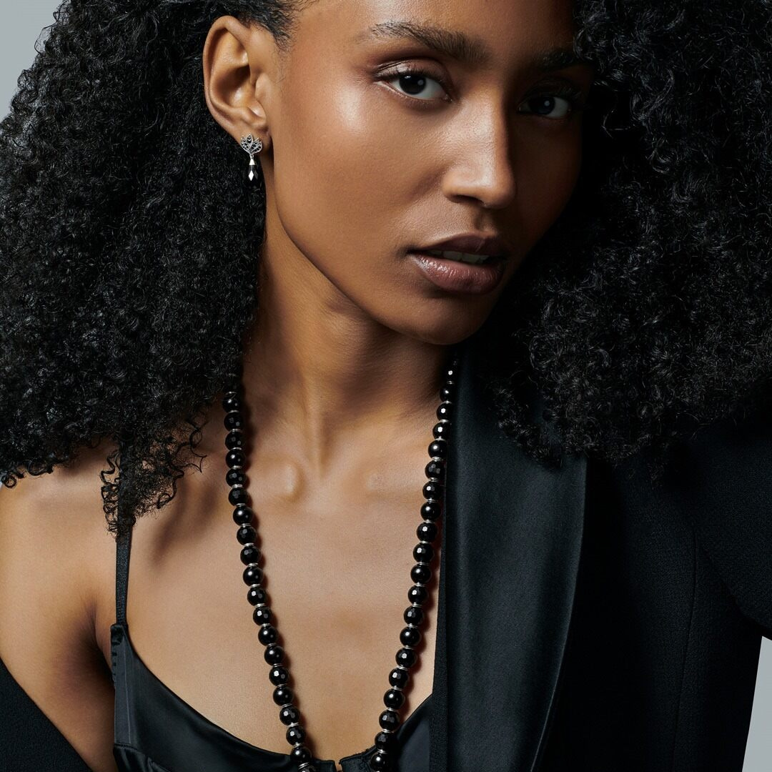 Woman seen from behind showcasing a THOMAS SABO crystal-pavé cross pendant necklace and silver bracelets, with dark hair and arm tattoo.