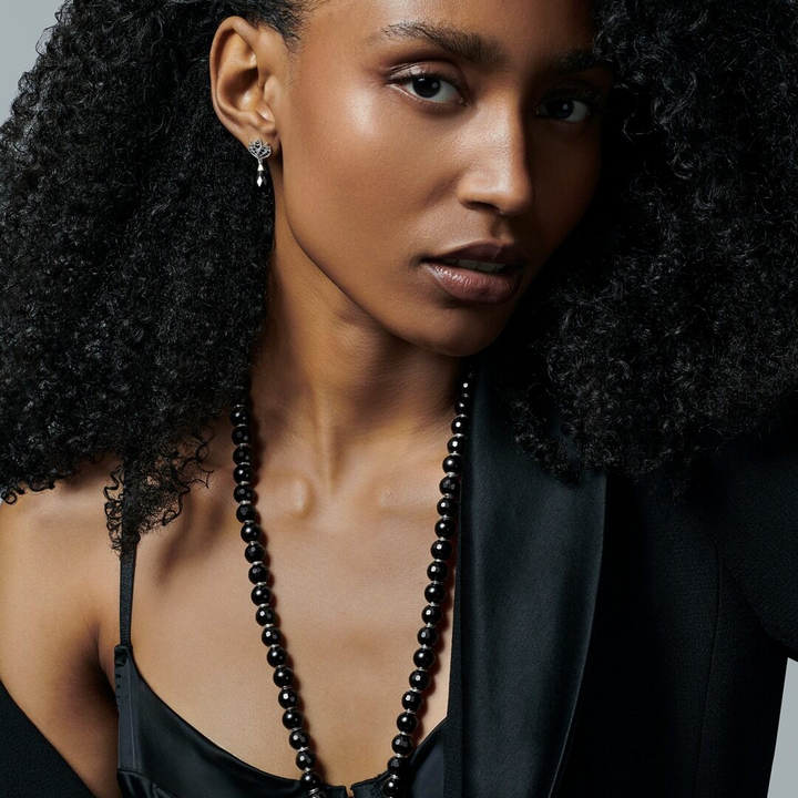 Woman seen from behind showcasing a THOMAS SABO crystal-pavé cross pendant necklace and silver bracelets, with dark hair and arm tattoo.