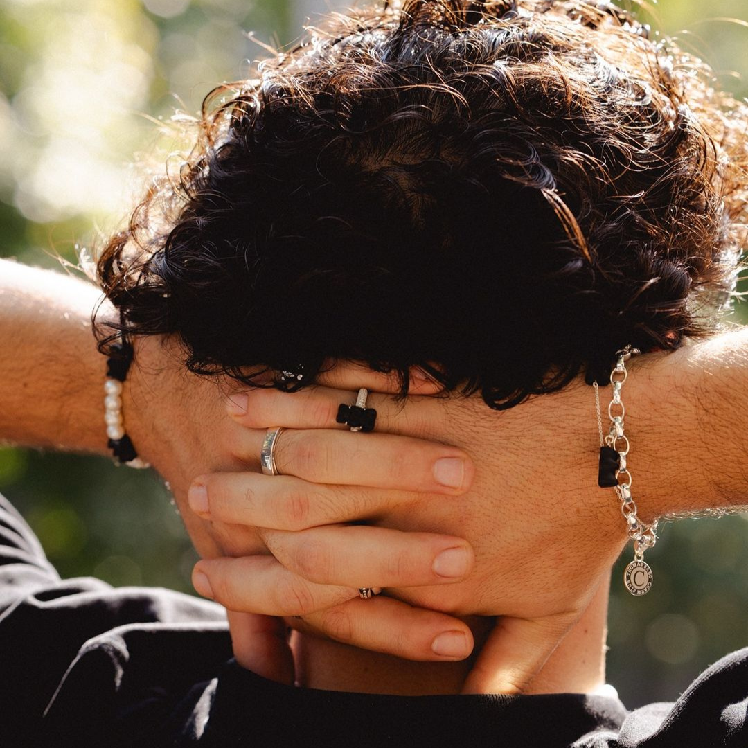 Woman seen from behind showcasing a THOMAS SABO crystal-pavé cross pendant necklace and silver bracelets, with dark hair and arm tattoo.