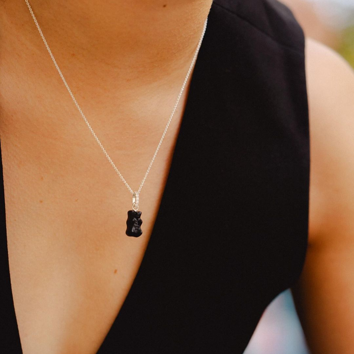 Woman seen from behind showcasing a THOMAS SABO crystal-pavé cross pendant necklace and silver bracelets, with dark hair and arm tattoo.