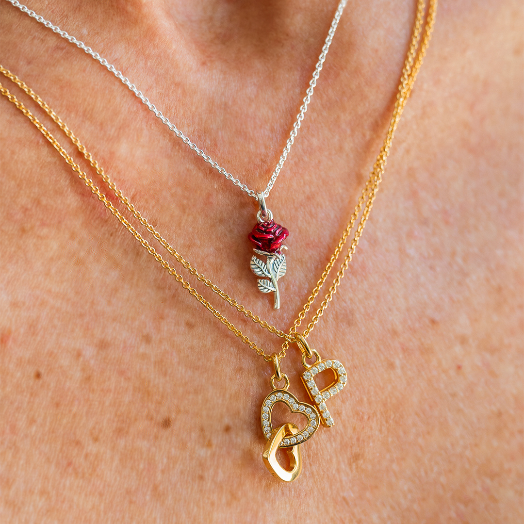 Woman seen from behind showcasing a THOMAS SABO crystal-pavé cross pendant necklace and silver bracelets, with dark hair and arm tattoo.