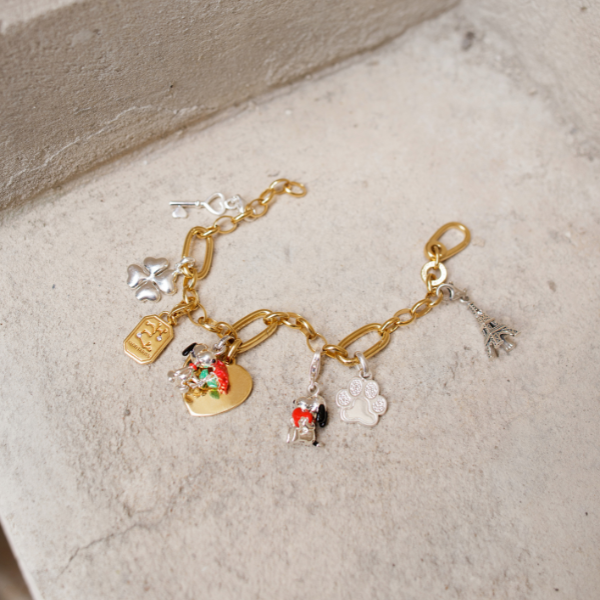 Two hands clasped together wearing THOMAS SABO yellow gold and sterling silver rings, bracelet, and crown pendant necklace; 