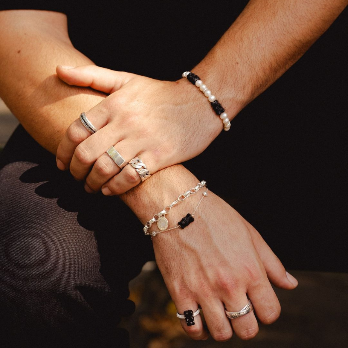 Two hands clasped together wearing THOMAS SABO yellow gold and sterling silver rings, bracelet, and crown pendant necklace; "Together" campaign.
